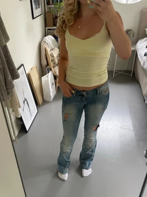 Ljusblå bootcut jeans - Säljer ett par lågmidjade ljusblå bootcut jeans med slitningar och hål. Jeansen är omgjorda från skinny till bootcut med lim som ska hålla tvätt. W27 L34