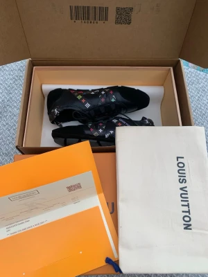 Louis Vuitton svarta sneakers - Louis Vuitton sneakers i svart läder med färgglada monogramdetaljer i rött, grönt, blått, vitt och gult. Skorna har låga skaft, snörning och robust sula. Ikonisk LV-logga på sidan och klassisk design som sticker ut.