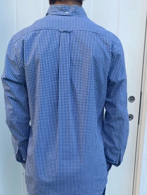 Blårutig gant skjorta  - Snygg blårutig skjorta från gant  med klassisk krage och vita knappar framtill. Skjortan har lång ärm och en liten broderad detalj på bröstet. Tillverkad i mjuk bomull som känns skön mot huden. Perfekt för dig som gillar en clean och stilren look.