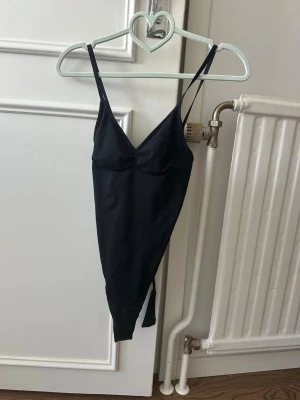 Svart body från H&M med smala band - Säljer en svart body från H&M med smala axelband och lätt v-ringad urringning. Bodyn är i stretchigt material och har en enkel, stilren design som passar perfekt till olika outfits. Superenkel att matcha och riktigt snygg! Ser liten ut men är självkart stretch i! I storlek S
