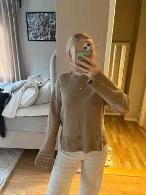 Other story tröja - Mysig beige stickad tröja med rund halsringning och breda ribbstickade muddar vid ärmslut och nederkant. Tröjan har en avslappnad passform och är perfekt för lager på lager under kyliga dagar. Materialet ser ut att vara mjukt och skönt.