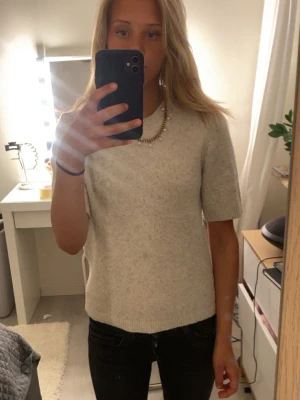 Beige stickad t-shirt med kort ärm - Säljer en beige stickad t-shirt med korta ärmar och rund hals. Tröjan har en enkel och clean design med ribbstickade kanter vid hals och nederkant. Perfekt för lager på lager och funkar året runt. Materialet ser mjukt och lite fluffigt ut💗