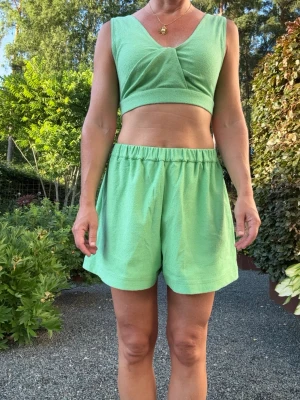 Sommar-set i grönt från Cos, shorts och topp - Snygga ljusgröna shorts med loose fit och elastisk midja. Shortsen har en enkel design med en bakficka. Kommer med tillhörande snygg bra-topp med veckade detaljer. Allt är tillverkat i ett mjukt boucle tyg som känns skönt mot huden. Perfekta för varma dagar och chill stunder utomhus vid poolen. Nytt skick, använt en eller två gånger. Köpt för 890 kr.