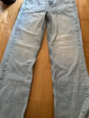 Ljusblå raka jeans - Säljer ett par ljusblå jeans med rak passform och klassisk femficksdesign. Jeansen har en tvättad look och är tillverkade i denim. Perfekta för dig som gillar en avslappnad och trendig stil. Storlek 38 men passar även 36