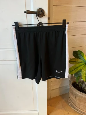 Svarta sportshorts Nike - Svarta fotbolls shorts från Nike, strl 147-158 L finns en liten reva bak, men annars fint skick!