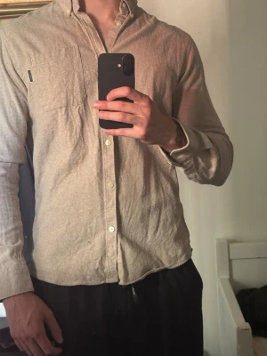 Beige skjorta från Lindbergh - Säljer en stilren beige skjorta med klassisk krage och knäppning framtill. Skjortan har en bröstficka och långa ärmar. Perfekt för dig som gillar en enkel och clean look.