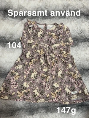 Ljuslila klänning med djurmönster - Supersöt ljuslila klänning med tryck av kaniner, ekorrar och blommor i vitt, beige och grönt. perfekt för vår och sommar. 🌸Sparsamt använd. Ej hellång ärm. Storlek 104