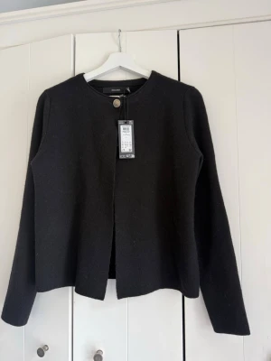 Svart cardigan från Vero Moda - Stilren svart cardiganjacka från Vero Moda med rund halsringning och en dekorativ knapp upptill. Aldrig använd med lapp kvar. 
