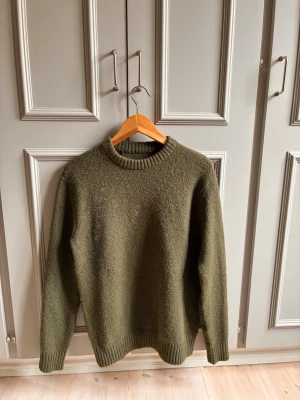 Olivgrön stickad tröja unisex - En enkel och stilren olivgrön stickad tröja med rund halsringning och ribbade muddar vid ärmslut och nederkant. Perfekt för lager på lager och passar till det mesta. Materialet känns mjukt och värmande.