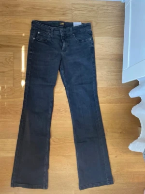 Svarta bootcut jeans från Lee - Snygga svarta jeans från Lee med bootcut-passform och klassisk femficksdesign. Jeansen har normal midja och raka ben som blir något utsvängda nertill. Perfekta för en avslappnad och trendig look.