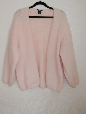 Ljusrosa stickad kofta - Mysig ljusrosa stickad kofta med öppen front och lång ärm. Koftan har en avslappnad passform och är perfekt för lager på lager. Supermjuk och fluffig känsla som ger en trendig look.
