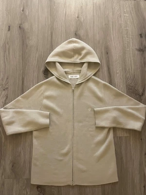 Samsøe Samsøe Saniklas Hoodie Moonstruck - Snygg beige hoodie från Samsøe Samsøe med dragkedja framtill och huva. Tillverkad i mjukt material och har en minimalistisk design med diskret logga på bröstet. Perfekt för en avslappnad och stilren look.