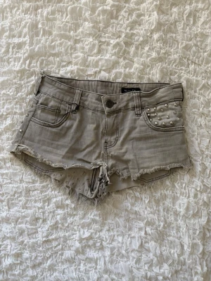 Massimo Dutti gråa jeansshorts med nitar och råa kanter - Supercoola gråa denimshorts med snygga nitdetaljer fram på ena fickan samt baktill runt ena bakfickan och linningen. Shortsen har en tuff, lite rockig stil med slitna och råa fransade kanter nertill. Från märket Massimo Dutti, i storlek 40. Midjemåttet rakt över är 36cm (alla mått finns i bilderna). Jättesnygga till sommaren! ✨