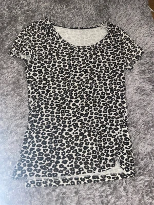 Leopardmönstrad t-shirt i svart och vit - Snygg t-shirt med leopardmönster i svart och vit. Modellen är klassisk med rund halsringning och korta ärmar. Perfekt för dig som vill sticka ut lite extra i vardagen. Materialet känns mjukt och följsamt mot kroppen.