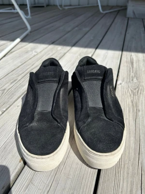 Svarta slip-on sneakers Axel Arigato - Svarta Axel Arigato skor i storlek 38, fortfarande väldigt fint omhändertagande. Inte mycket som tyder på att de är slitna. Box ingår inte, önskar man däremot skostöd för att de ska behålla sin form under hela leveransen fixar jag det! 