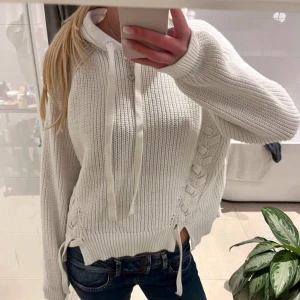 Vit stickad hoodie med snörning - Säljer en vit stickad hoodie med snörning i sidan och huva med dragsko. Tröjan har ribbade muddar och avslappnad passform, perfekt för en chill och trendig look. Passar till jeans eller leggings. Storlek s lite oversized 💓