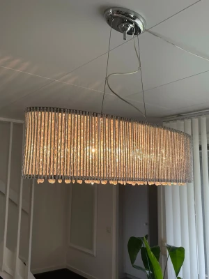 Oval kristall lampa  - Säljer en stor, oval taklampa med kristallprismor och silverfärgad ram. Lampan har en elegant och lyxig design med hängande kristaller som reflekterar ljuset snyggt. Perfekt som statement piece över matbordet eller i vardagsrummet.