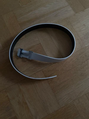  vitt/svart bälte med silverdetalj - Säljer ett vitt bälte med en snygg silverfärgad metallspänne. Bältet har en clean och modern look, perfekt för att lyfta vilken outfit som helst. Materialet känns slätt och bältet är smalt med klassisk design.