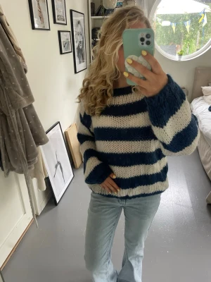 Randig blåvit stickad tröja - Mysig stickad tröja med breda marinblå och vita ränder. Tröjan har en avslappnad passform, långa ärmar och grovstickad struktur. Perfekt för dig som gillar en chill och trendig look. .