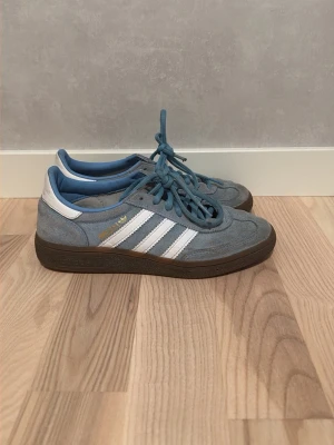 Blå adidas spezial - Snygga blå sneakers från Adidas med klassiska vita ränder på sidorna och brun sula. Skorna har ovandel i mocka och detaljer i vitt läder. Perfekta för en avslappnad streetstyle-look.