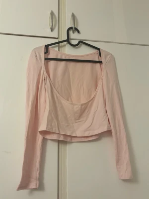 Ljusrosa långärmad topp med öppen rygg - Säljer en ljusrosa croppad topp med lång ärm och djup öppen rygg. Toppen har en enkel och stilren design som passar perfekt till jeans eller kjol. Tillverkad i mjukt bomullsmaterial för en bekväm känsla.