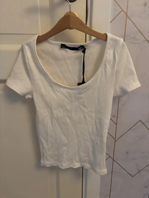Vit ribbad kortärmad topp - Snygg vit ribbad topp med korta ärmar och djup rundringning. Tillverkad i mjuk bomull som känns skön mot huden. Perfekt att matcha med jeans eller kjol för en clean look.