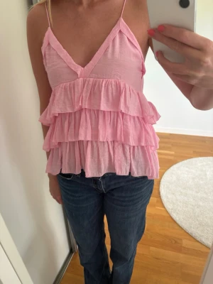 Rosa volangtop zara - Supersöt rosa linnetopp med flera volanger och tunna axelband. Toppen har v-ringning och är ärmlös. Nästan aldrig använd! Storlek xs men passar även s