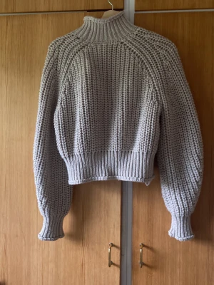 Beige  chunky stickad tröja - Säljer en beige chunky stickad tröja med hög krage och breda ribbade muddar. Tröjan har  ä grovstickad struktur som ger en cool och avslappnad look. Perfekt för lager på lager under kyliga dagar.