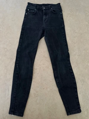 Svarta skinny jeans med dragkedja - Säljer ett par svarta skinny jeans med dragkedja vid benslutet. Jeansen har klassisk femficksmodell och hög midja. Materialet är stretchigt för en bekväm passform och de har en snygg tvättad look. Perfekta till sneakers eller boots.