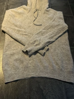 Ljusgrå merinó ull hoodie - Säljer en ljusgrå hoodie i mjukt material med ribbade muddar vid ärmslut och nederkant. Hoodien har en klassisk huva med dragsko och lång ärm. Perfekt för dig som gillar en enkel och clean stil. Har använts 2-3 gånger. Inge defekter