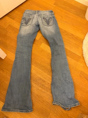 Ljusblå bootcut jeans med slitningar - Säljer ett par ljusblå bootcut jeans med slitningar framtill och broderade detaljer på bakfickorna. Nästan helt nya. Sitter bra för någon som vill ha låg midja på sina jeans. 