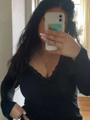 Svart långärmad topp med spets från Nelly - Snygg svart långärmad topp från Nelly med v-ringning och spetsdetaljer längs urringningen. 