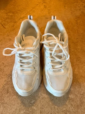 Chunky vita sneakers med meshdetaljer - Säljer ett par chunky vita sneakers med tjock sula och meshdetaljer. Skorna har snörning och sportig design med inslag av syntetmaterial och textil. Perfekta för dig som gillar en trendig och clean look.