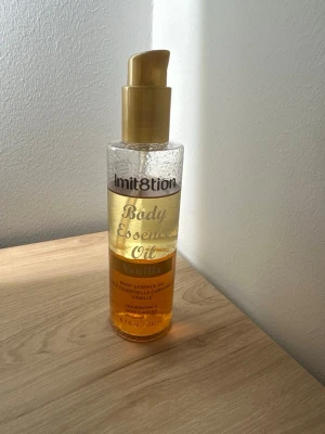 Body Essence Oil Vanilla Imit8tion - Lyxig kroppsolja med vaniljdoft från Imit8tion. Kommer i en genomskinlig plastflaska med guldfärgad pump och etikett. Oljan är gyllene och ger näring till huden. Perfekt för dig som vill ha en mjuk och väldoftande hud.