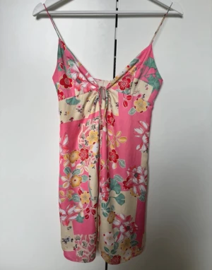 Blommig kort klänning från Zara - Söt kort klänning från Zara med tunna axelband och färgglatt blommönster i rosa, beige, gul och grönt. Klänningen har snörning framtill och är perfekt för varma dagar. Tillverkad i ett lätt och mjukt material.