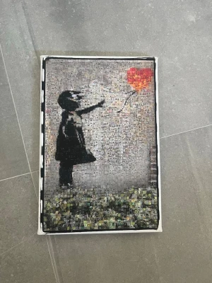 Tavla med Banksy-motiv Ballongflicka - Tavla som föreställer Banksys ikoniska Ballongflicka. Motivet är sammansatt av många små bilder som tillsammans skapar en mosaik i svart, grått och rött. Perfekt som dekoration eller konstnärlig detalj till rummet.