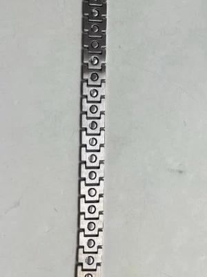 Silvrigt länkarmband i metall - Säljer ett stilrent armband i silverfärgad metall med rektangulära länkar. Ena sidan har ett geometriskt mönster med cirklar, medan andra sidan har ett rutigt, texturerat mönster. Perfekt för dig som gillar en clean och modern look.