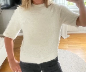 Vit fluffig stickad tröja - Mysig vit stickad tröja med korta ärmar och hög hals. Tröjan har en fluffig textur och rak passform, perfekt för dig som gillar en enkel men trendig look. Passar till både jeans och kjol.