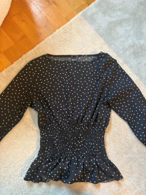 Svart prickig tröja  - Svart långärmad tröja från Gina Tricot med vita prickar och smockad midja som ger en snygg siluett. Tillverkad i ett mjukt och stretchigt material. Perfekt för dig som gillar trendiga mönster.
