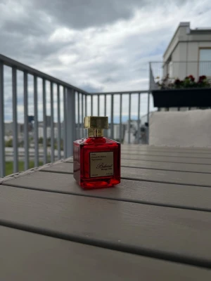 Röd parfymflaska Baccarat rouge 540 - Snygg parfym från Baccarat rouge 540 i en fyrkantig röd glasflaska med guldfärgat lock. Flaskan rymmer 100 ml och har en elegant etikett framtill. Doften heter Bakhour och är Eau de Parfum, tillverkad i Förenade Arabemiraten. Perfekt för dig som gillar exklusiva och orientaliska dofter.