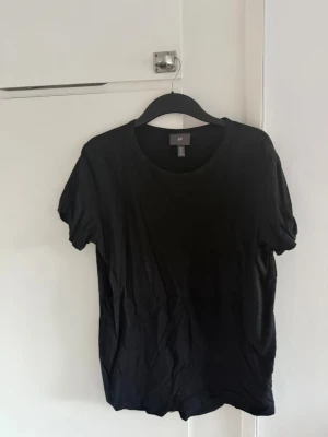Svart basic t-shirt från H&M - En klassisk svart t-shirt från H&M med rund halsringning och korta ärmar. Perfekt att matcha med jeans eller shorts. Tillverkad i mjuk bomull för en skön känsla hela dagen.
