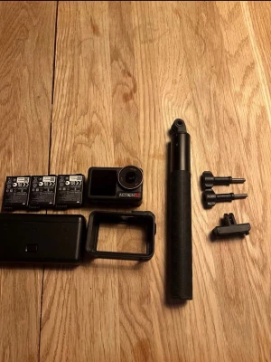 DJI Action 5 Pro med tillbehör - Säljer en svart Action 5 Pro actionkamera. Medföljer tre batterier, skyddsfodral, ram, selfiestick och fästen. Perfekt för dig som vill filma äventyr och sport. Kameran är kompakt och har robust design i plast.