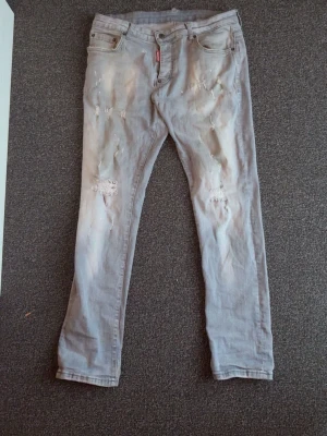 Disquared Ljusgrå slitna jeans med hål - Säljer ett par ljusgrå jeans med skinny fit och slitningar samt hål på framsidan. Jeansen har klassisk femficksmodell och knappgylf. Perfekta för dig som gillar en avslappnad och trendig stil.