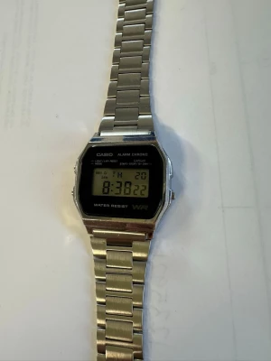 Digital klocka i silver från Casio - Klassisk digital klocka från Casio med silverfärgad metallarmband och svart digital display. Klockan har funktioner som alarm, kronograf och datumvisning. Stilren och retro design som passar till många olika stilar.