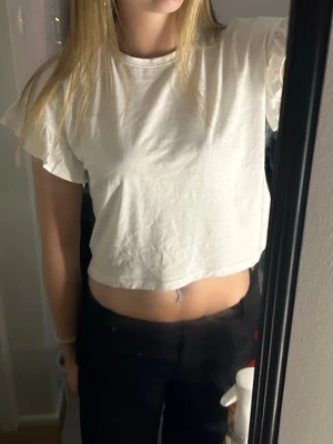Vit croppad t-shirt - En enkel vit croppad t-shirt med korta ärmar och rund hals. Perfekt till jeans eller kjol för en avslappnad look. Tillverkad i mjukt bomullsmaterial som känns skönt mot huden.