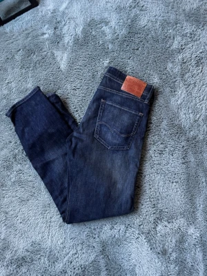 Mörkblå tapered jeans från Jack & Jones - Snygga mörkblå jeans från Jack & Jones i modellen Tapered Mike. Jeansen har klassisk femficksdesign, kontrastsömmar och en skinnpatch bak i midjan. Perfekta för dig som gillar en smalare passform med lite mer utrymme upptill.
