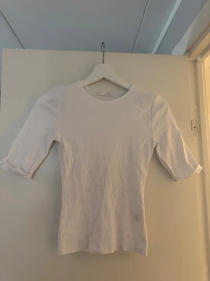 Vit t-shirt med trekvartsärm - En enkel och stilren vit t-shirt med trekvartsärm och rund halsringning. T-shirten har en smal passform och är tillverkad i mjuk bomull, perfekt för en clean och fräsch look.