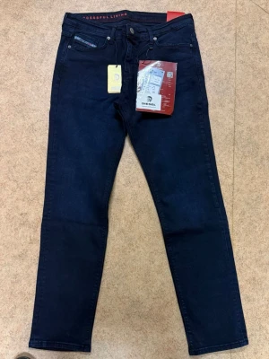 Mörkblå slim fit jeans från Diesel - Snygga mörkblå slim fit jeans från Diesel med klassisk femficksdesign och diskreta detaljer. Jeansen har en modern passform och är tillverkade i ett stretchigt denimtyg för extra komfort. Perfekta för dig som gillar stilrena och trendiga jeans.
