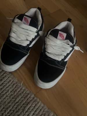 Svarta och vita Vans Old Skool sneakers - Klassiska Vans Old Skool sneakers i svart och vitt med vit sula och breda vita skosnören. Skorna har den ikoniska sidostripen och kontrastsömmar. Ovandelen är i canvas och mocka för en tidlös streetstil.