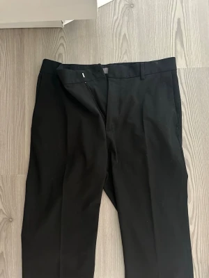 Svarta kostymbyxor H&M Slim Fit - Snygga svarta kostymbyxor från H&M i modellen Slim Fit. Byxorna har klassisk design med raka ben, bälteshällor och sidofickor. Materialet känns mjukt och följsamt. Storlek 175/eur 30